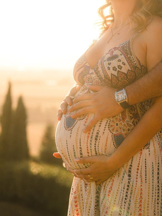 Pareja abrazando la barriga de embarazo a contraluz al atardecer