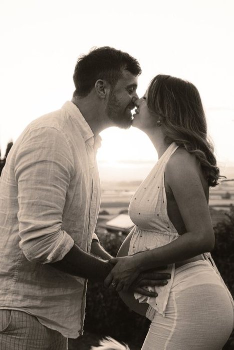 Pareja besándose a contraluz durante una sesión de embarazo, en blanco y negro